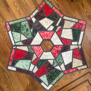 Peut inclure: Une courtepointe en patchwork rouge, verte et blanche en forme d'étoile. La courtepointe est faite de différents tissus avec des motifs et des textures différents. La courtepointe est parfaite pour une jupe de sapin de Noël.