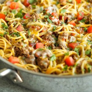 May include: A close-up of a skillet filled with a cheesy pasta dish topped with ground beef, diced tomatoes, and fresh parsley.