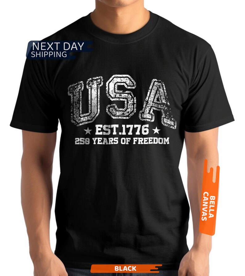 Peut inclure: T-shirt noir avec un motif blanc vieilli indiquant "USA EST. 1776 250 YEARS OF FREEDOM". Le t-shirt a un col rond et semble &ecirc;tre en coton.