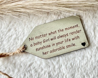 May include: A wooden tag with a twine string, featuring the text "No matter what the moment, a baby Girl will always render sunshine in your life with her adorable smile."