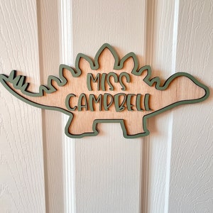 May include: A wooden dinosaur cutout with a green outline. The dinosaur has the text "Miss Campbell" written on it.