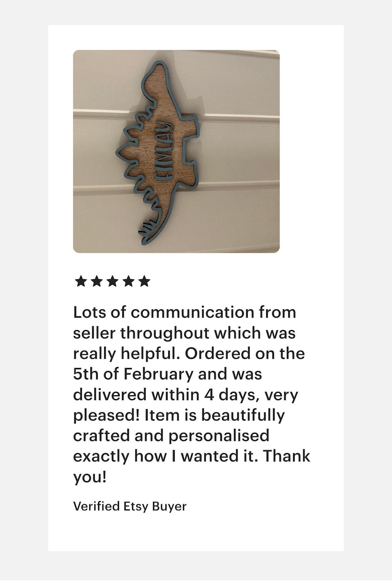 May include: A wooden dinosaur cutout with a blue outline. The dinosaur's name, "FIMLAY", is written on the cutout in a light blue font.
