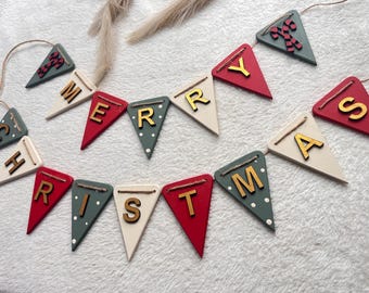 May include: A decorative banner featuring triangular pennants in red, white, and sage green, strung together with twine. The pennants display the gold-colored letters spelling MERRY CHRISTMAS, with additional pennants featuring candy cane motifs.