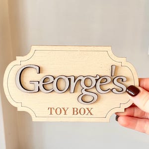 May include: A wooden toy box sign with the name "George's" in raised letters and the words "TOY BOX" below.