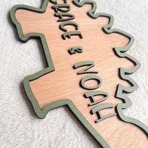 May include: A wooden dinosaur-shaped sign with a green outline. The sign says "GRACE & NOAH" in a green cursive font.