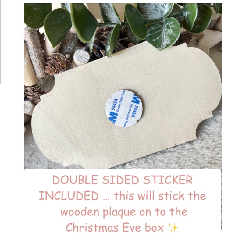 May include: A close-up of a wooden plaque with a double-sided sticker attached to the back. The sticker is labeled "9448A Double Coated Tissue". The text "DOUBLE SIDED STICKER INCLUDED... this will stick the wooden plaque on to the Christmas Eve box" is written below the image.