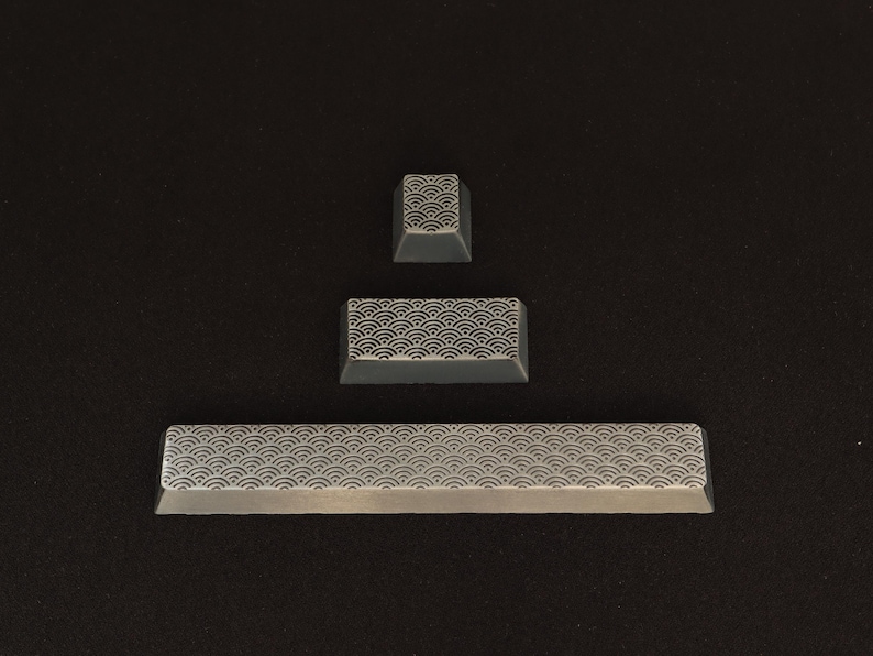 May include: Three gray keyboard keycaps with a repeating wave pattern. The keycaps are arranged in a vertical line, with a small square keycap at the top, a rectangular keycap in the middle, and a long rectangular keycap at the bottom.