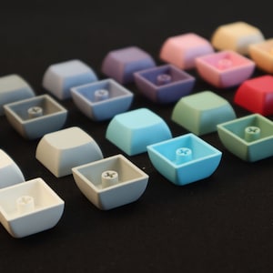 May include: A collection of colorful keycaps in various shades of blue, green, purple, pink, red, and gray. The keycaps are arranged in rows on a black surface.