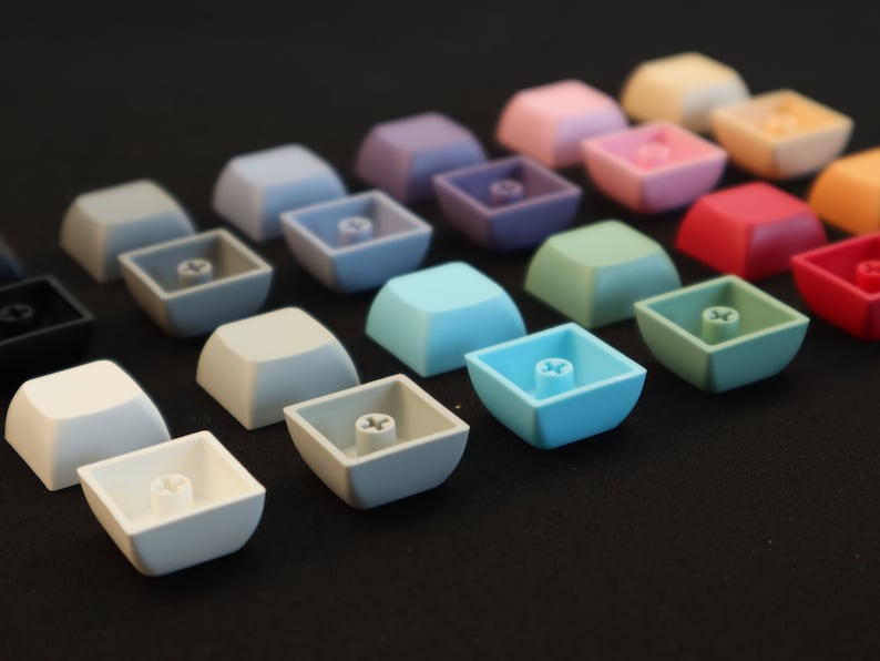 May include: A collection of colorful keycaps in various shades of blue, green, purple, pink, red, and gray. The keycaps are arranged in rows on a black surface.