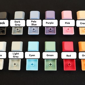 May include: A set of 12 keycaps in various colors, including black, white, light grey, dark grey, pale blue, cyan, green, purple, pink, cream, red, and orange. Each keycap has a plus sign printed on it.
