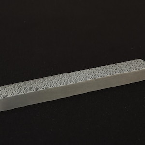 May include: A rectangular, light gray keyboard keycap with a repeating wave pattern in a darker gray. The keycap is angled and appears to be made of a solid material. The background is a solid black.