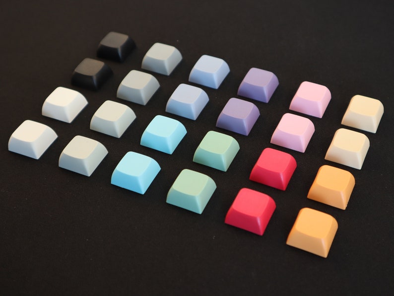 May include: A collection of 18 square keycaps in various colors, including black, gray, light blue, green, pink, red, orange, and yellow. The keycaps are arranged in a triangular pattern on a black surface.