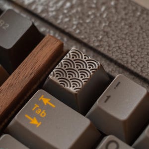 May include: Close-up of a mechanical keyboard with custom keycaps. The Tab key is gray with yellow arrows and the word "Tab". The space bar is a dark wood. The keycap has a repeating wave pattern.