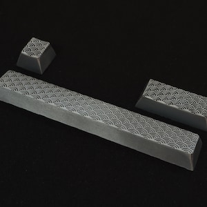 May include: Gray keyboard keycaps with a repeating wave pattern. The set includes a long spacebar key and two smaller keys. The design is a light gray on a darker gray background.