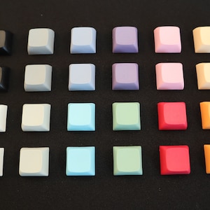 May include: A set of 20 keycaps in various colors, including black, white, gray, blue, green, purple, pink, orange, and red. The keycaps are arranged in a grid pattern on a black surface.