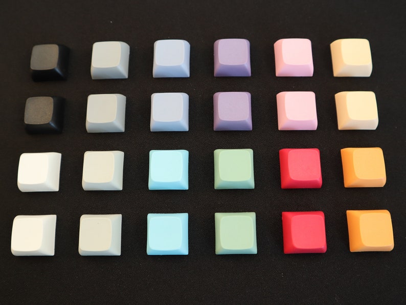 May include: A set of 20 keycaps in various colors, including black, white, gray, blue, green, purple, pink, orange, and red. The keycaps are arranged in a grid pattern on a black surface.