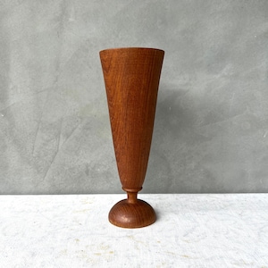 Puede incluir: Un jarrón de madera con forma cónica acampanada y base redonda. El jarrón está hecho de madera marrón oscura con un veteado natural.