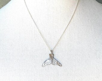 Op de afbeelding: Een zilveren ketting met een getextureerde walvisstaart hanger.