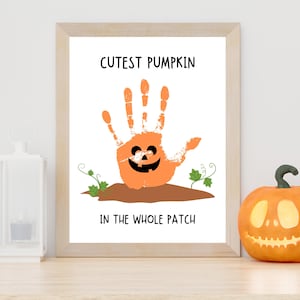 K&ouml;nnte beinhalten: Ein gerahmter Druck mit einem orangefarbenen Handabdruck in K&uuml;rbisform und einem schwarzen Jack-o'-Lantern-Gesicht. Der Text lautet CUTEST PUMPKIN IN THE WHOLE PATCH. Das Design zeigt braune Erde und kleine gr&uuml;ne Ranken auf wei&szlig;em Hintergrund.