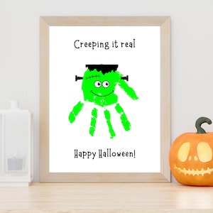 K&ouml;nnte beinhalten: Ein gerahmter Druck mit einem leuchtend gr&uuml;nen Handabdruck, der als Monster mit schwarzen Haaren, Bolzen und Augen gestaltet ist. Der Text lautet Creeping it real oben und Happy Halloween! unten, alles auf einem klaren wei&szlig;en Hintergrund.
