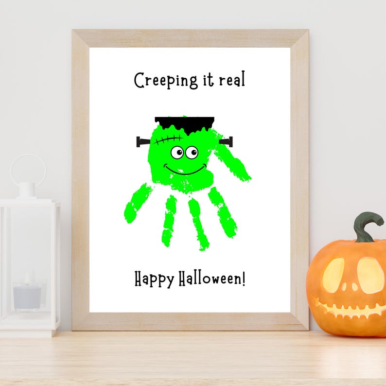 K&ouml;nnte beinhalten: Ein gerahmter Druck mit einem leuchtend gr&uuml;nen Handabdruck, der als Monster mit schwarzen Haaren, Bolzen und Augen gestaltet ist. Der Text lautet Creeping it real oben und Happy Halloween! unten, alles auf einem klaren wei&szlig;en Hintergrund.