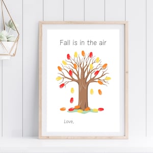 May include: A framed print with a white background featuring a brown tree with red, orange, and yellow leaves. The text "Fall is in the air" is above the tree and the text "Love," is below the tree.