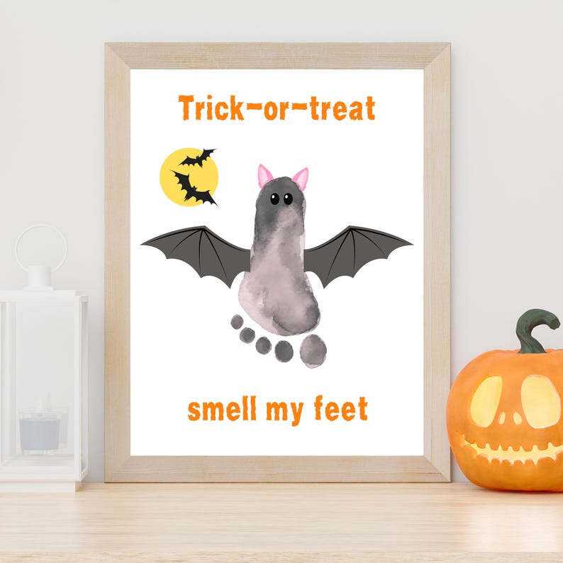 K&ouml;nnte beinhalten: Ein gerahmter Druck mit einem grauen Fu&szlig;abdruck, der als Fledermaus mit schwarzen Fl&uuml;geln, rosa Ohren und zwei Augen gestaltet ist. Der orangefarbene Text Trick-or-treat und smell my feet steht dar&uuml;ber und darunter. Ein gelber Mond ist zu sehen.