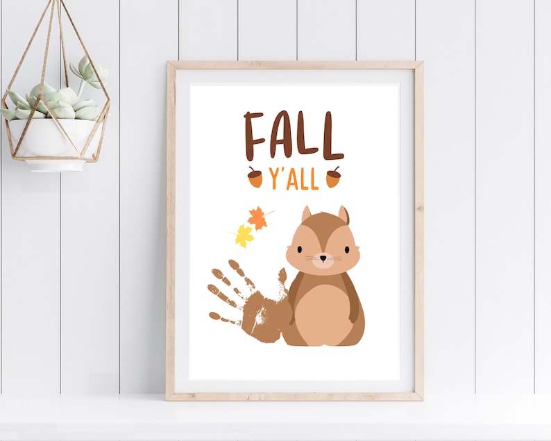 May include: A printable art print with a brown squirrel and the text "Fall Y'all" with two acorns on either side of the text. There are also three orange and yellow leaves in the top left corner of the print.