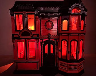 May include: A red and black miniature Victorian-style house with illuminated windows. The house features intricate architectural details, including a decorative roof, ornate trim, and a front door. The windows glow with a warm, inviting light, creating a spooky ambiance.