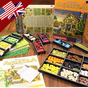 Puede incluir: Un organizador de tablero de juego para el juego de mesa Agricola. El organizador está hecho de plástico negro y tiene múltiples compartimentos para guardar los componentes del juego. El organizador se muestra con la caja del juego y otros componentes, incluyendo meeples de madera, cartas y fichas.