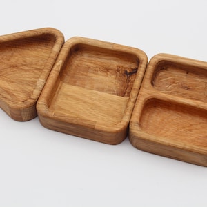 Könnte beinhalten: Drei Serviertabletts aus Holz in verschiedenen Formen: ein Dreieck, ein Rechteck und ein Rechteck mit zwei Fächern. Die Tabletts sind aus hellbraunem Holz mit sichtbarer Maserung gefertigt, was eine natürliche, rustikale Ästhetik suggeriert. Ideal zum Servieren von Snacks oder kleinen Artikeln.