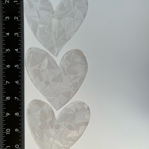 Puede incluir: Tres pegatinas transparentes en forma de coraz&oacute;n con un patr&oacute;n similar a un mosaico. Las pegatinas est&aacute;n dispuestas verticalmente sobre un fondo blanco. Una regla se coloca junto a las pegatinas, mostrando medidas en cent&iacute;metros.