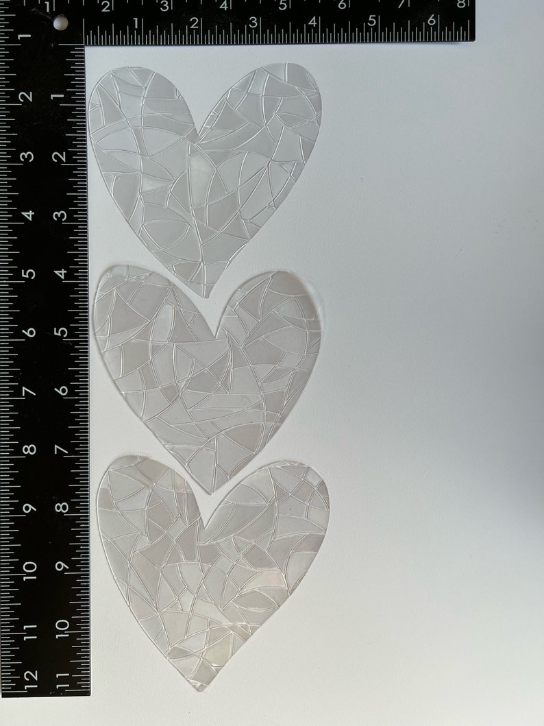 Puede incluir: Tres pegatinas transparentes en forma de coraz&oacute;n con un patr&oacute;n similar a un mosaico. Las pegatinas est&aacute;n dispuestas verticalmente sobre un fondo blanco. Una regla se coloca junto a las pegatinas, mostrando medidas en cent&iacute;metros.