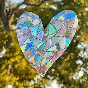 Puede incluir: Un adhesivo para ventana en forma de coraz&oacute;n con efecto vidriera. El adhesivo est&aacute; hecho de material iridiscente, que refleja un espectro de colores, incluyendo azul, verde y rosa. El dise&ntilde;o est&aacute; compuesto por formas geom&eacute;tricas irregulares.