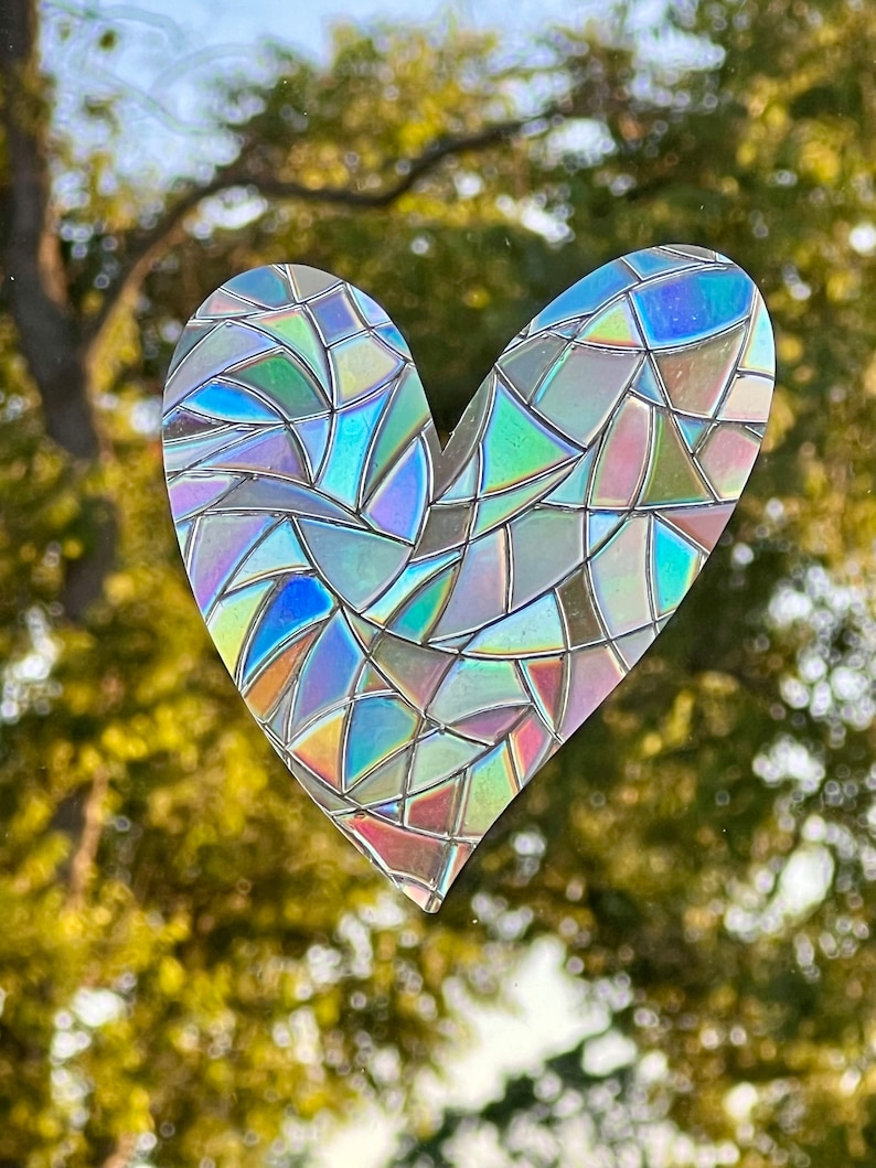 Puede incluir: Un adhesivo para ventana en forma de coraz&oacute;n con efecto vidriera. El adhesivo est&aacute; hecho de material iridiscente, que refleja un espectro de colores, incluyendo azul, verde y rosa. El dise&ntilde;o est&aacute; compuesto por formas geom&eacute;tricas irregulares.
