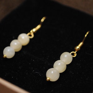 Peut inclure: Une paire de boucles d'oreilles en or avec trois perles blanches nacrées sur chaque boucle d'oreille.