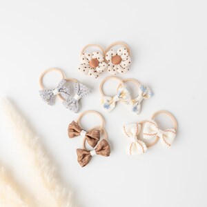 May include: A set of six hair bows in various colors and patterns, including floral, polka dot, and solid colors. The bows are attached to elastic hair ties.