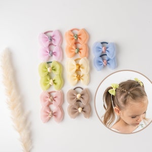 May include: Set of ten pastel-colored hair bows with double bows. Each bow is made of soft, sheer fabric and has a small flower accent in the center. The bows are attached to elastic hair ties.
