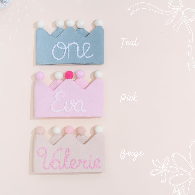 May include: Three felt crowns in teal, pink, and beige, each with a different name embroidered in white or pink. The teal crown says "one", the pink crown says "Eva", and the beige crown says "Valerie". Each crown has pom-poms.