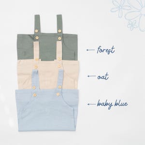 May include: Three sleeveless rompers stacked vertically in forest green, oat beige, and baby blue. Each romper features two shoulder straps with light-colored wooden buttons. Text labels indicate the colors as forest, oat, and baby blue.