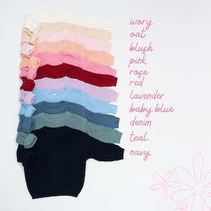 May include: A stack of ribbed knit sweaters in various colors, including ivory, oat, blush, pink, rose, red, lavender, baby blue, denim, teal, and navy. The sweaters are neatly arranged on a white background, with color names written in pink script.