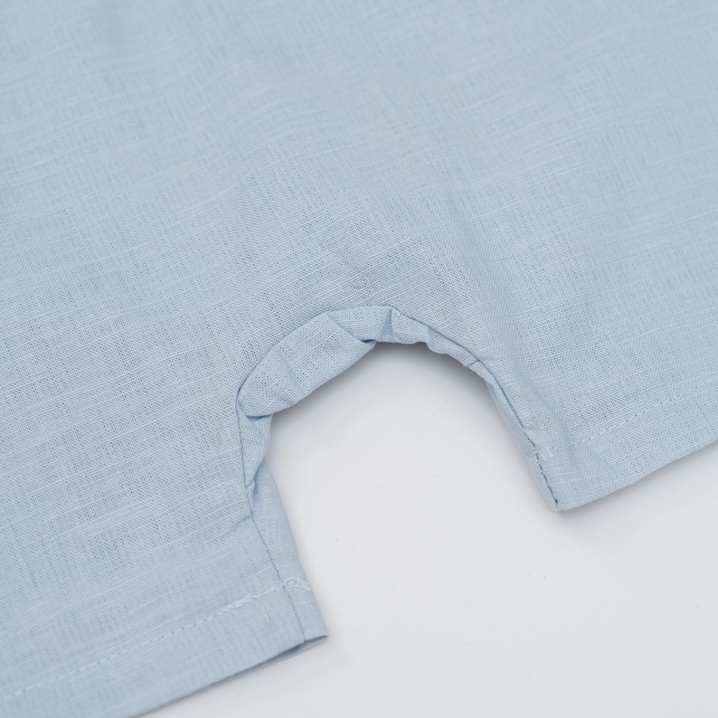 May include: A light blue garment featuring a woven texture and a curved cutout section. The fabric displays a visible cross-hatch pattern with straight stitched seams along the edges of the opening and the hemline of the textile material.