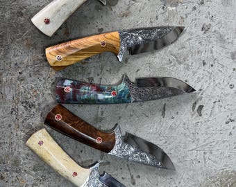 以下が含まれることがあります： 彫刻された刃を持つ5つのカスタムナイフの品揃え。 ハンドルは、明るい骨、木目、大理石模様など、色と素材が異なります。 各ナイフは装飾的なリベットと研磨仕上げが特徴です。