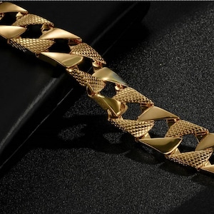 May include: A gold-toned chain bracelet featuring thick, interlocking links. Each link displays a dual-texture design, alternating between a smooth, polished surface and a textured, cross-hatched pattern that catches the light across the metal.