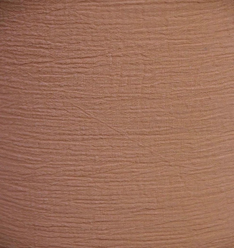 May include: A solid light brown fabric featuring a distinct horizontal crinkled texture throughout the surface. The material displays a consistent earthy tan colour with fine, parallel ridges that create a subtle, rippled visual effect across the entire textile.
