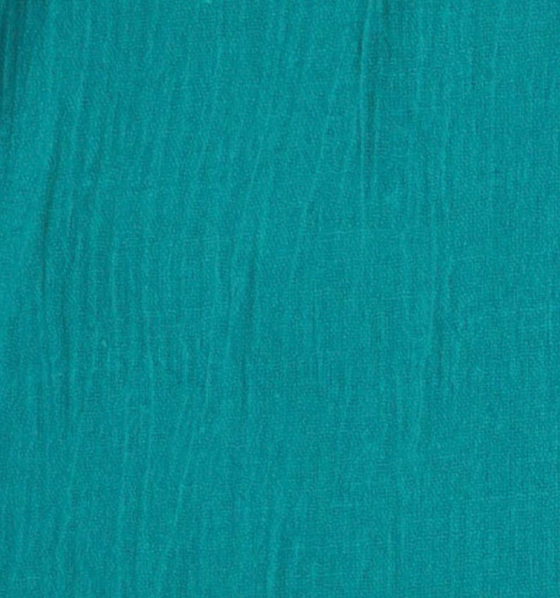 May include: A solid teal fabric with a distinct crinkled, textured surface. The material displays a consistent deep blue-green colour throughout, featuring vertical folds and a lightweight, woven appearance that creates subtle shadows across the textile.