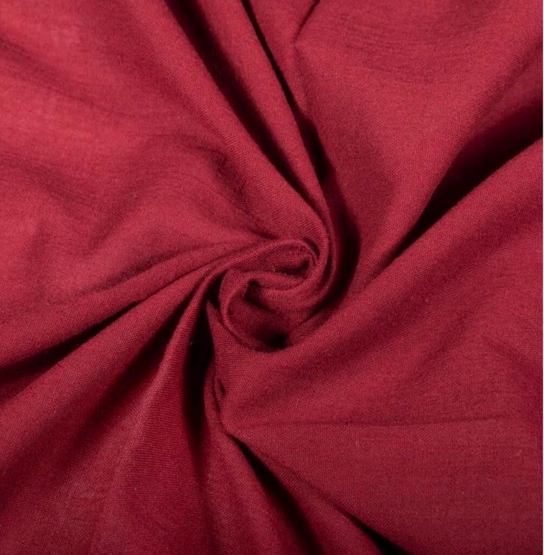 May include: A deep burgundy fabric with a soft, matte texture, featuring natural folds and creases that create a dynamic play of light and shadow across the surface. The material appears lightweight and flexible, showing a consistent solid colour.