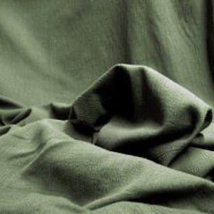 May include: A solid olive green fabric with a visible woven texture, draped in soft, cascading folds that create deep shadows and highlights across the surface, emphasising the natural movement and matte finish of the textile material.