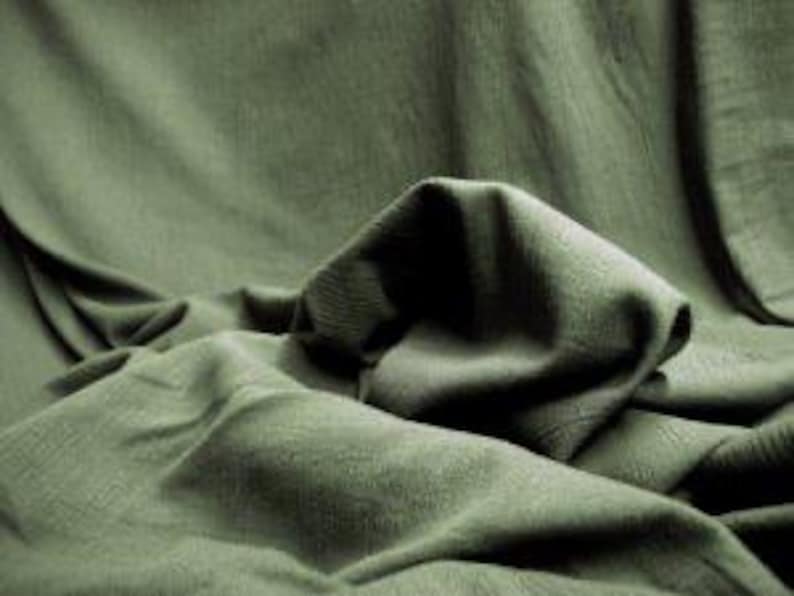 May include: A solid olive green fabric with a visible woven texture, draped in soft, cascading folds that create deep shadows and highlights across the surface, emphasising the natural movement and matte finish of the textile material.