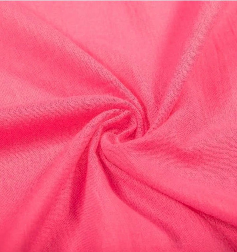 May include: A vibrant hot pink fabric with a soft, fine-knit texture. The material is gathered in the centre, creating natural folds and shadows that highlight the consistent, bright pink colour and the delicate, lightweight weave of the textile.